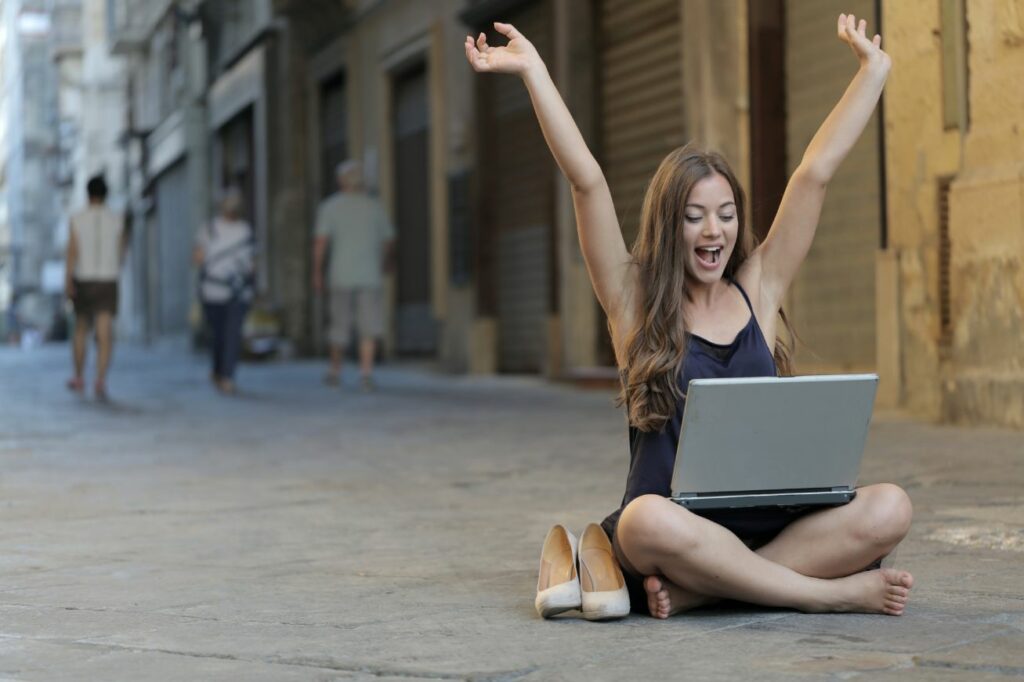 Young woman sitting in the street with her laptop on her lap.