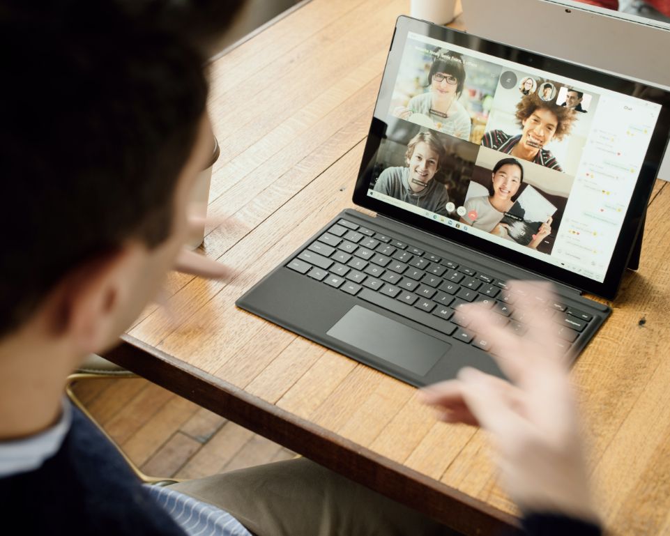 A video call with 4 people on screen and one person sitting on the laptop.