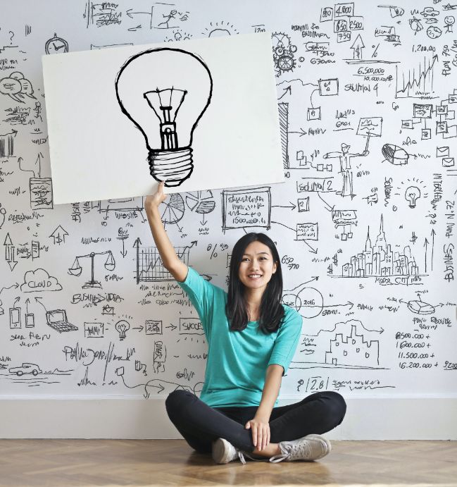 Woman sitting on the floor holding up a drawing of a light bulb